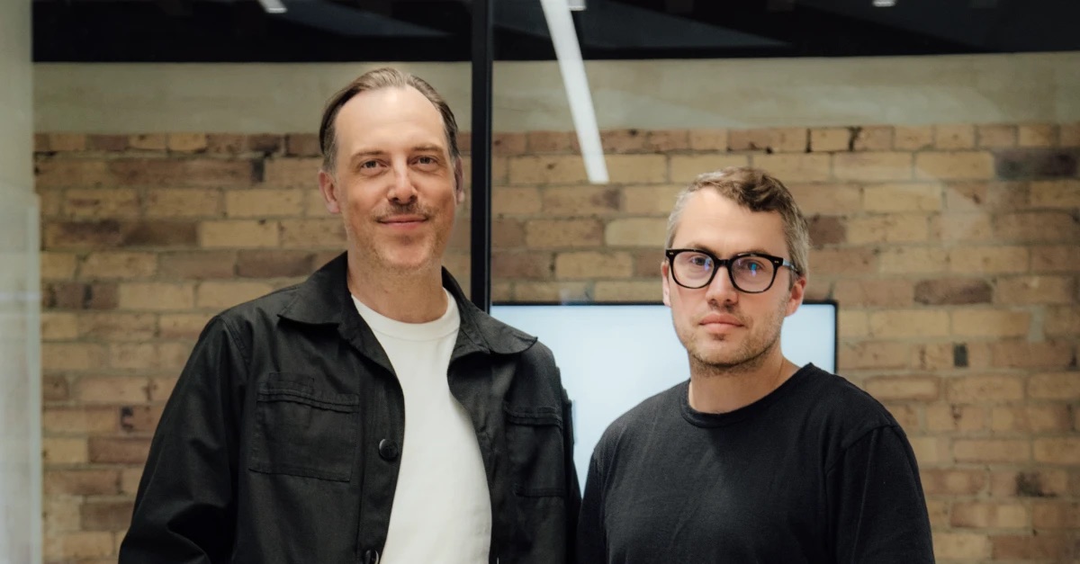 Barney Chunn, CEO and co-founder of Drumbeat (right), standing with a colleague in front of a brick wall